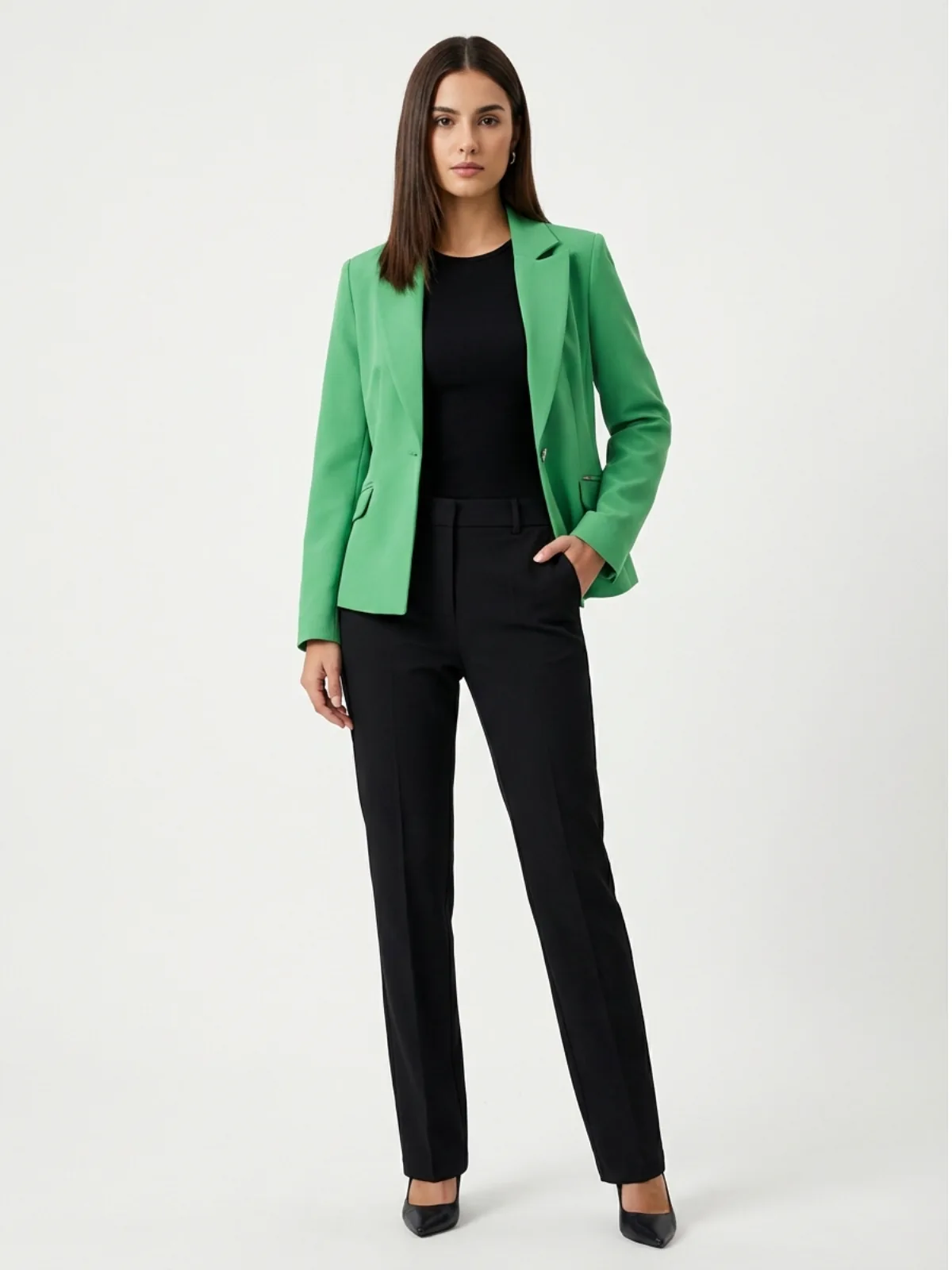 wirtualna modelka ubrana w zielony żakiet damski czarny top, czarne elegackie spodnie w kant oraz szpilki, trzyma ręce w kieszeni prezentując się na jasnym tle w studio