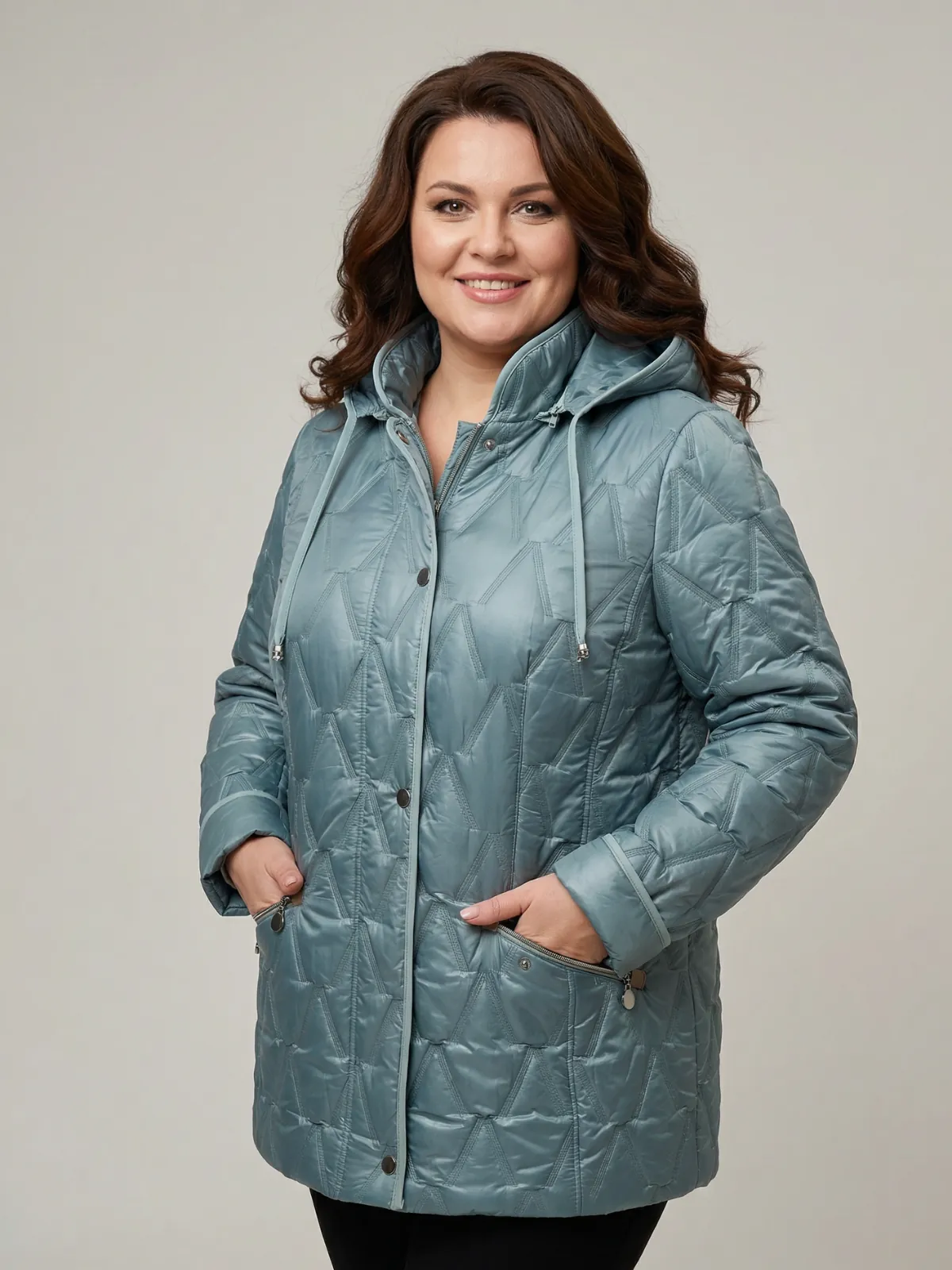 Modelka plus size o brązowych włosach prezentuje w studio kurtkę damską w kolorze miętowym w niestandardowe prasowanie w literę V, trzyma ręce w kieszeni i delikatnie sie uśmiecha