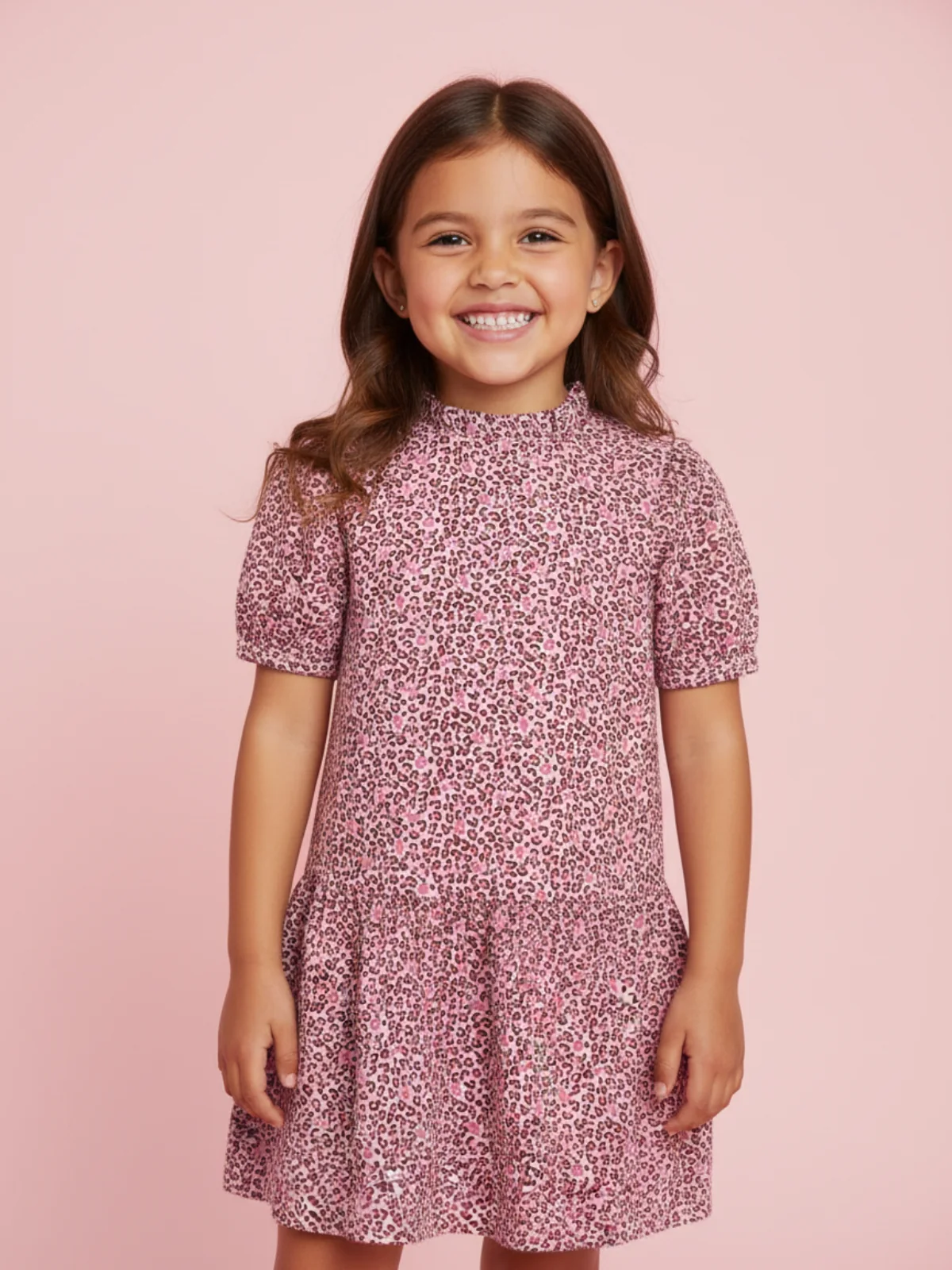 uśmiechnięta 7 letnia dziewycznka w sukience w cenki w kolorze różowym, stoi w studio na pastelowym tle