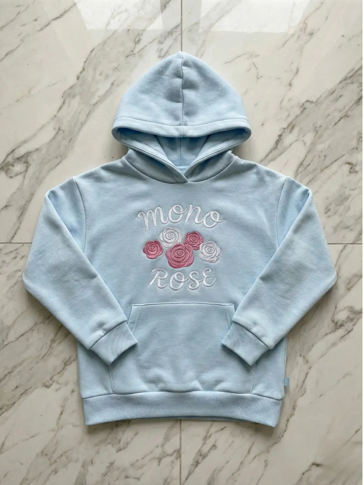 niebieska bluza w odcieniu baby blue z naszytym napisem monorose i grafikami bialo rozowych rozy lezy na podlodze, zdjeice robione z góry