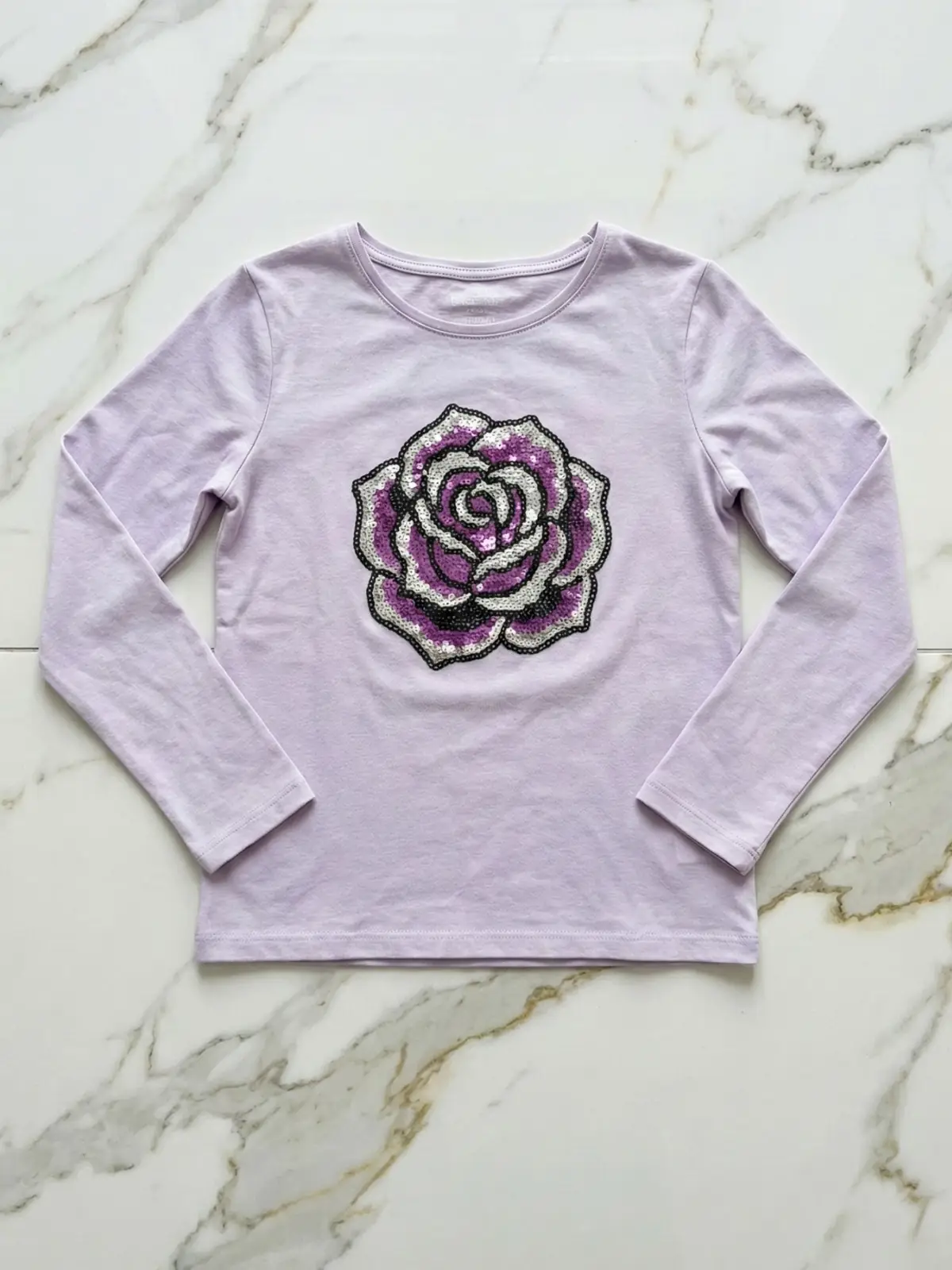 flatlay rozowej koszulki dzieciecej z ikona rozy na klatce piersiowej lezy na podlodze