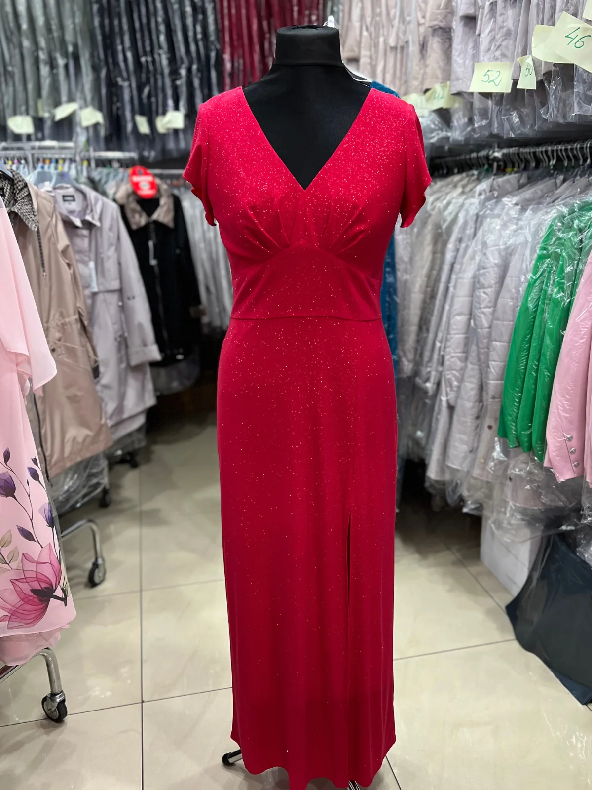 Odważna czerwona sukienka wieczorowa, długa podkreślona wykończeniem z brokatu, pokazana na manekinie w sklepie