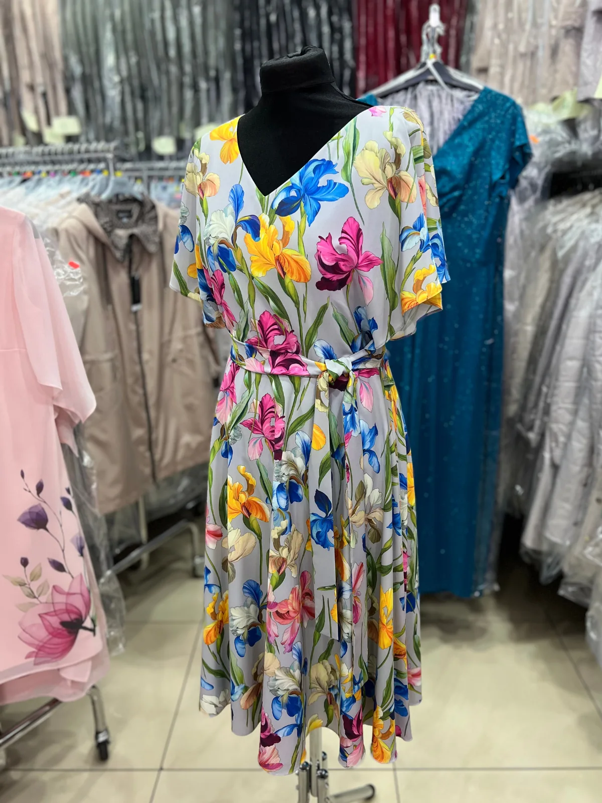 sukienka w kolorze szarym w print w kolorowe kwiatki, pokazana na czarnym manekinie w sklepie